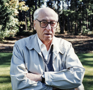 Photo of Gunther Gerzso waist up, dressed in his usual light blue wind breaker and grey Burberry sweater, wearing his black Swatch.
                                His expression is combination of inquisitiveness and sarcasm.